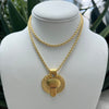 A gold double-strand necklace with a mushroom-shaped pendant, displayed on a white jewelry bust with blurred green foliage in the background.