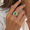 A gold signet ring with a rectangular green stone, worn on a woman's hand.