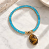 A gold-filled tennis bracelet with a circular arrangement of bright turquoise rectangular stones and a large oval tiger's eye pendant, displayed on a white marble surface.