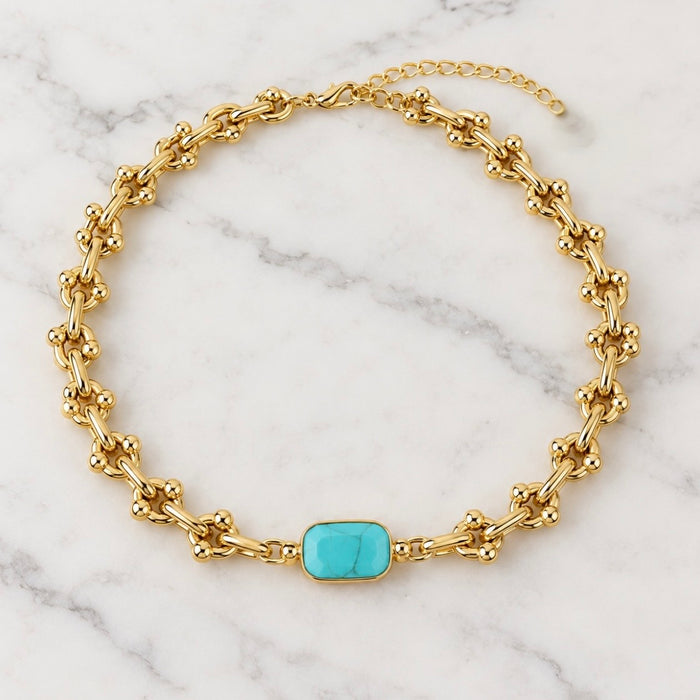 A gold chain necklace with a central turquoise rectangular stone, displayed on a white marble background.
