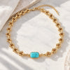 A gold chain necklace with a central rectangular turquoise stone, displayed on a white marble surface with soft shadows.