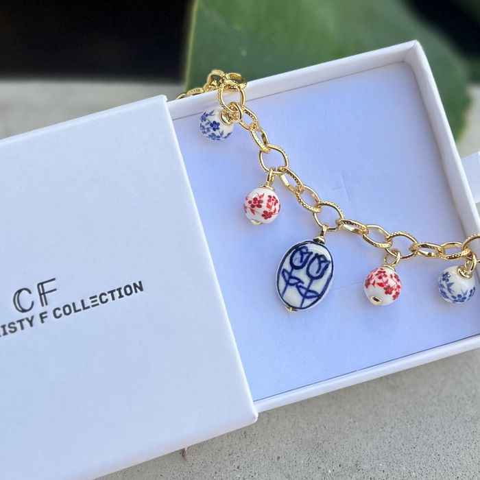 A gold-filled chain bracelet with ceramic floral charms displayed in an open white box with 'CF COLLECTION' inscribed.