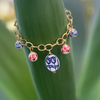 A gold-filled bracelet with ceramic floral charms displayed on a green stem.