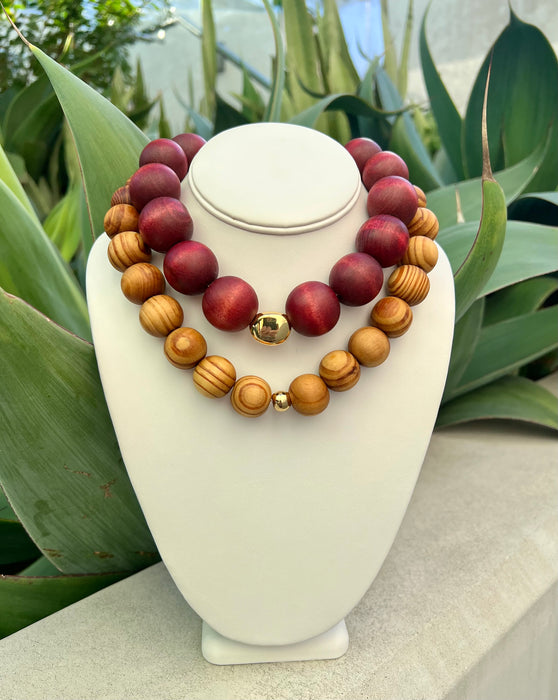 Wooden beaded necklace on a white stand with green leaves in the background