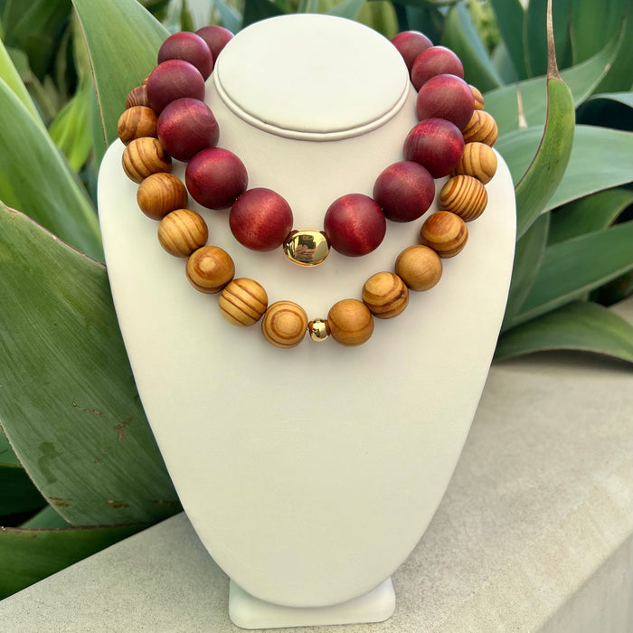 Wooden beaded necklace on a white stand with green leaves in the background
