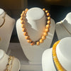Wooden beaded necklace on a white stand with gold chain necklace in the background.
