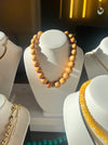 Wooden beaded necklace on a white stand with gold chain necklace in the background.