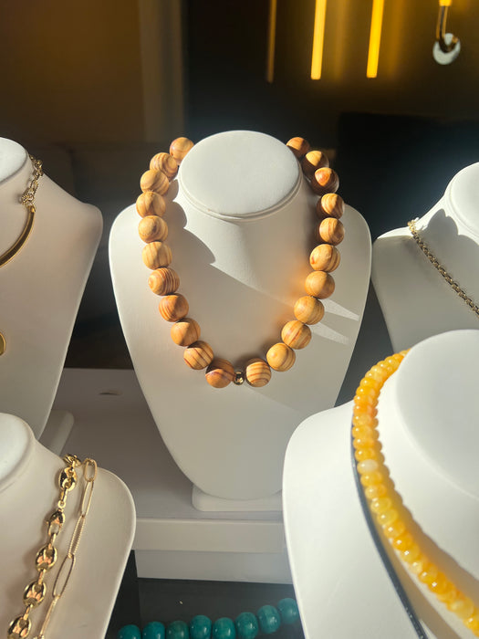 Wooden beaded necklace on a white stand with gold chain necklace in the background.