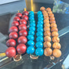 Three beaded necklaces in red, blue, and brown on a reflective surface.