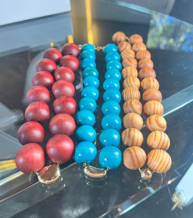 Three beaded necklaces in red, blue, and brown on a reflective surface.