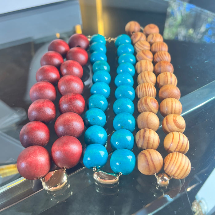 Three beaded necklaces in red, blue, and brown on a reflective surface.