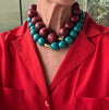 Person wearing a red jacket with a large turquoise and burgundy beaded necklace.