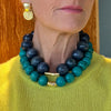 Person wearing a blue and green beaded necklace with a gold clasp.