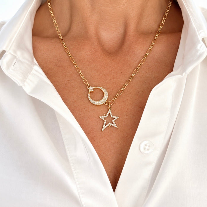A close-up of a model wearing a gold chain necklace with a small pavé-set crescent moon and a dangling pavé-set star pendant, styled with a white button-down shirt.