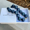 Blue beaded necklace in a white box with 'The Christy F Collection' branding on a concrete surface.
