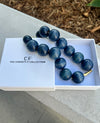 Blue beaded necklace in a white box with 'The Christy F Collection' branding on a concrete surface.