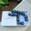 Blue beaded necklace in a white box with 'The Christy F. Collection' branding on a stone surface.
