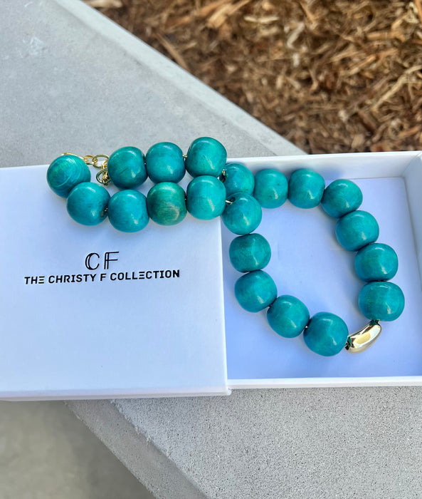 Turquoise beaded necklace with gold clasp on a white box labeled 'The Christy F Collection'.