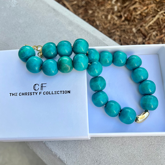 Turquoise beaded necklace with gold clasp on a white box labeled 'The Christy F Collection'.