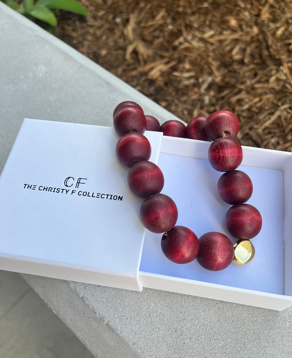 Wooden beaded necklace with a gold accent on a white box labeled 'The Christy F Collection'.