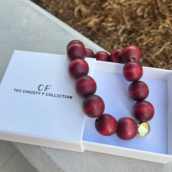 Wooden beaded necklace with a gold accent on a white box labeled 'The Christy F Collection'.