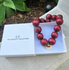 Necklace with red beads and gold clasp in a white box labeled 'The Christy F Collection'.