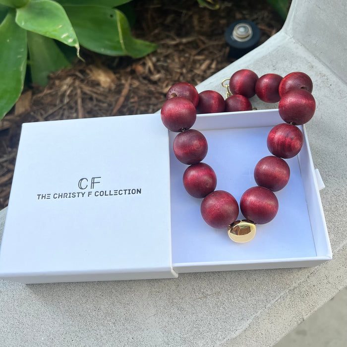 Necklace with red beads and gold clasp in a white box labeled 'The Christy F Collection'.