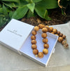 Wooden beaded necklace in a white box with 'The Christie Collection' branding, against a natural background.