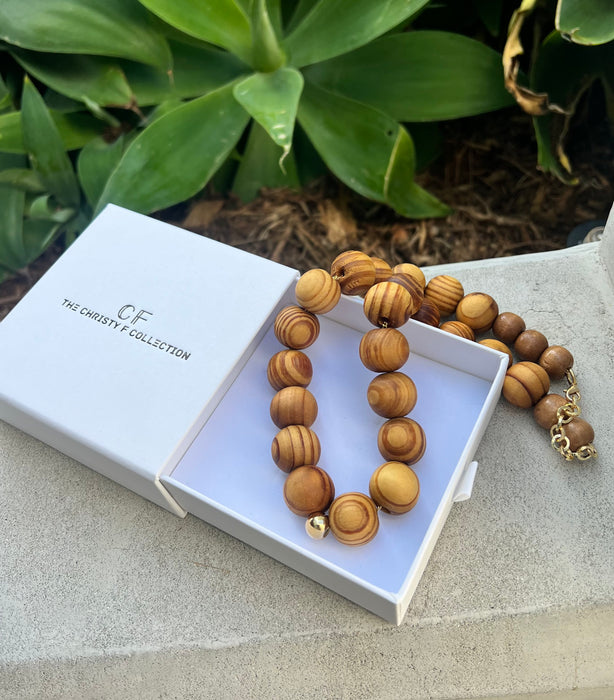 Wooden beaded necklace in a white box with 'The Christie Collection' branding, against a natural background.