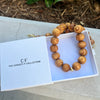 Wooden necklace in an open box with 'The Christy F Collection' branding on a concrete surface.