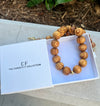 Wooden necklace in an open box with 'The Christy F Collection' branding on a concrete surface.