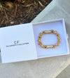 Gold bracelet in a box with 'The Christy F Collection' branding on a concrete surface.