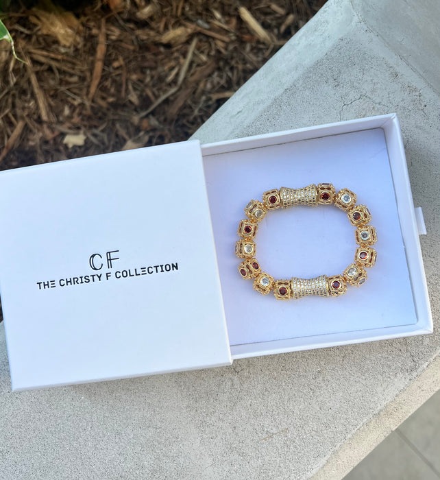 Gold bracelet in a box with 'The Christy F Collection' branding on a concrete surface.