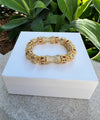 Gold bracelet with gemstones on a white box against a green plant background