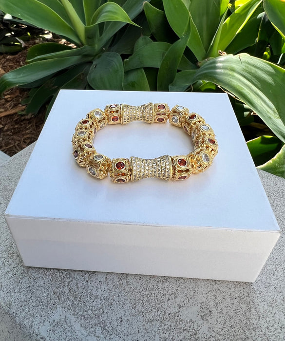 Gold bracelet with gemstones on a white box against a green plant background