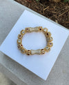 Gold bracelet with gemstones on a white square platform outdoors