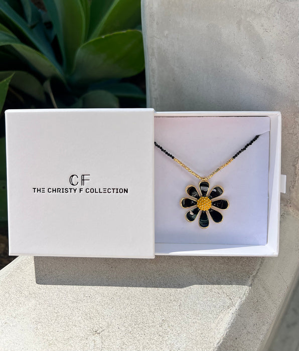 Floral necklace in a 'The Christy F Collection' box with a plant in the background