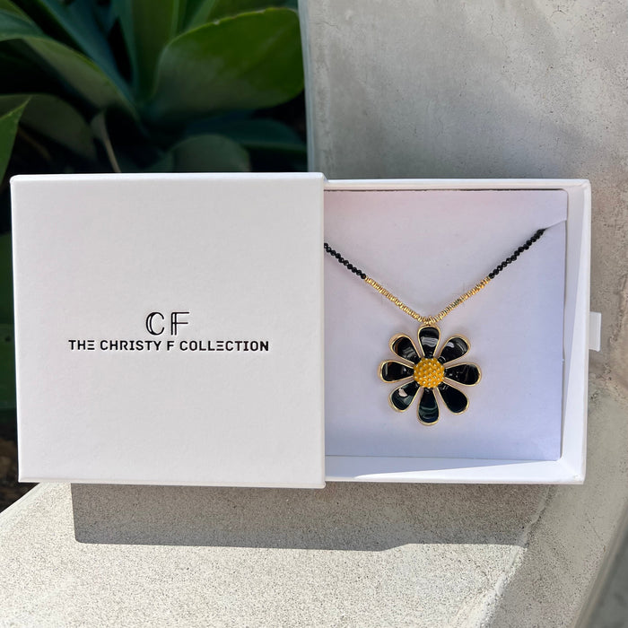 Floral necklace in a 'The Christy F Collection' box with a plant in the background