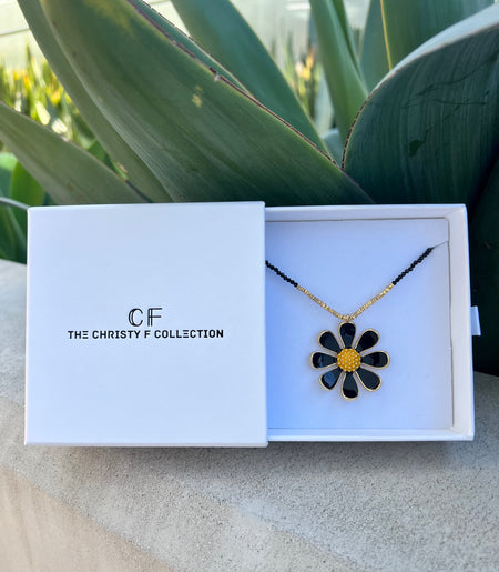 Floral necklace in a 'The Christy F Collection' box with plants in the background