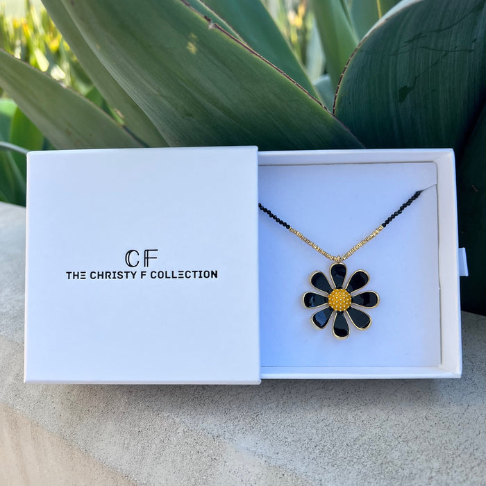 Floral necklace in a 'The Christy F Collection' box with plants in the background