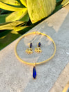 Gold necklace with blue pendant and matching earrings on a stone surface with green leaves in the background