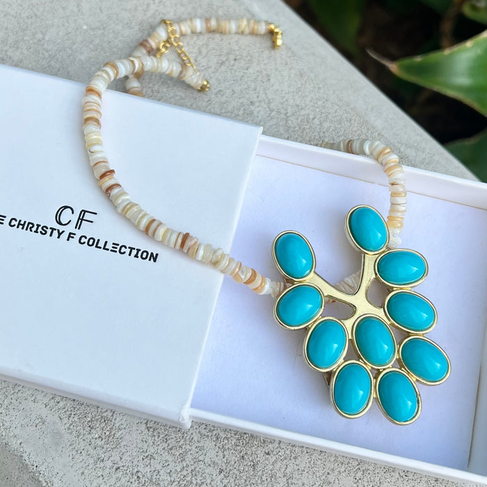 Necklace with turquoise pendant and beaded chain on a white box with 'CF' branding.