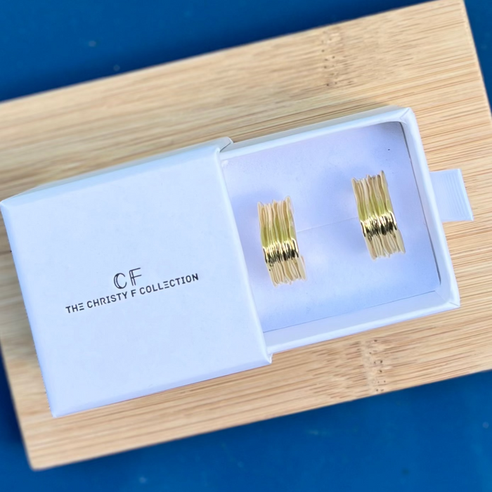 Gold earrings in a box with 'The Christy F Collection' branding on a blue background