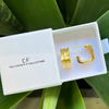 Gold hoop earrings in a 'The Christy F Collection' box with green leaves in the background