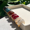 Set of colorful gemstone bracelets on a white surface with green foliage in the background
