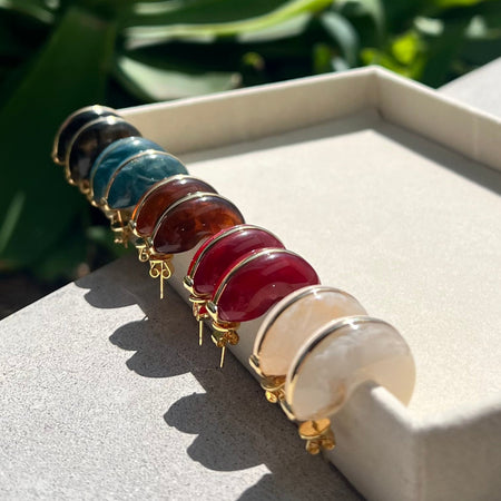 Set of colorful gemstone bracelets on a white surface with green foliage in the background
