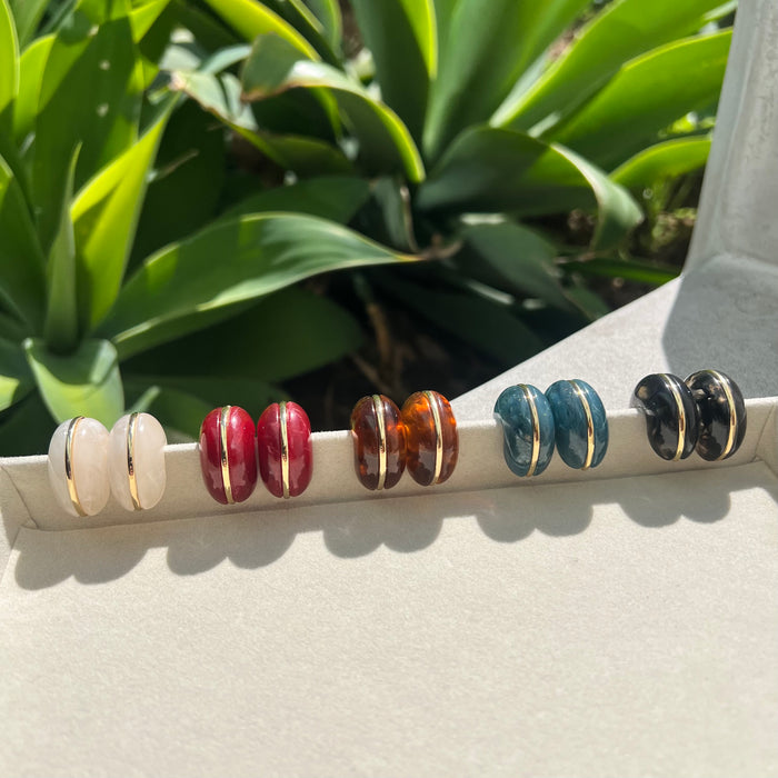 Set of colorful beaded hair ties on a white surface with green leaves in the background