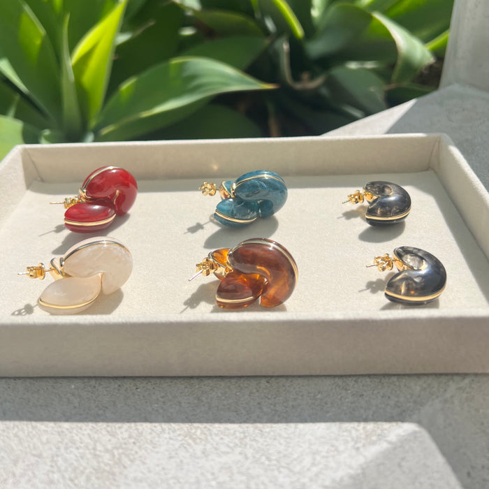 Set of colorful butterfly-shaped earrings on a white tray with a green plant background.