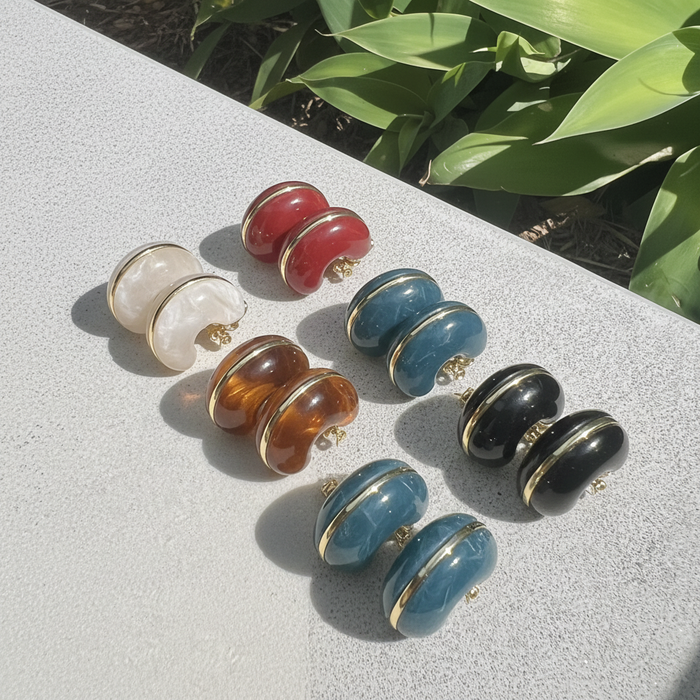 Set of colorful earrings on a textured surface with greenery in the background
