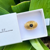 Gold ring with black gemstone in a white box labeled 'CF Collection' on green leaves.